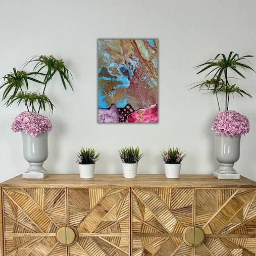 Decorative setup with a wooden cabinet, potted plants, and a colorful abstract painting on a white wall.