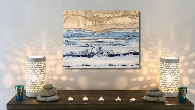 Decorative setup with a painting, candles, and lanterns on a shelf against a white wall.